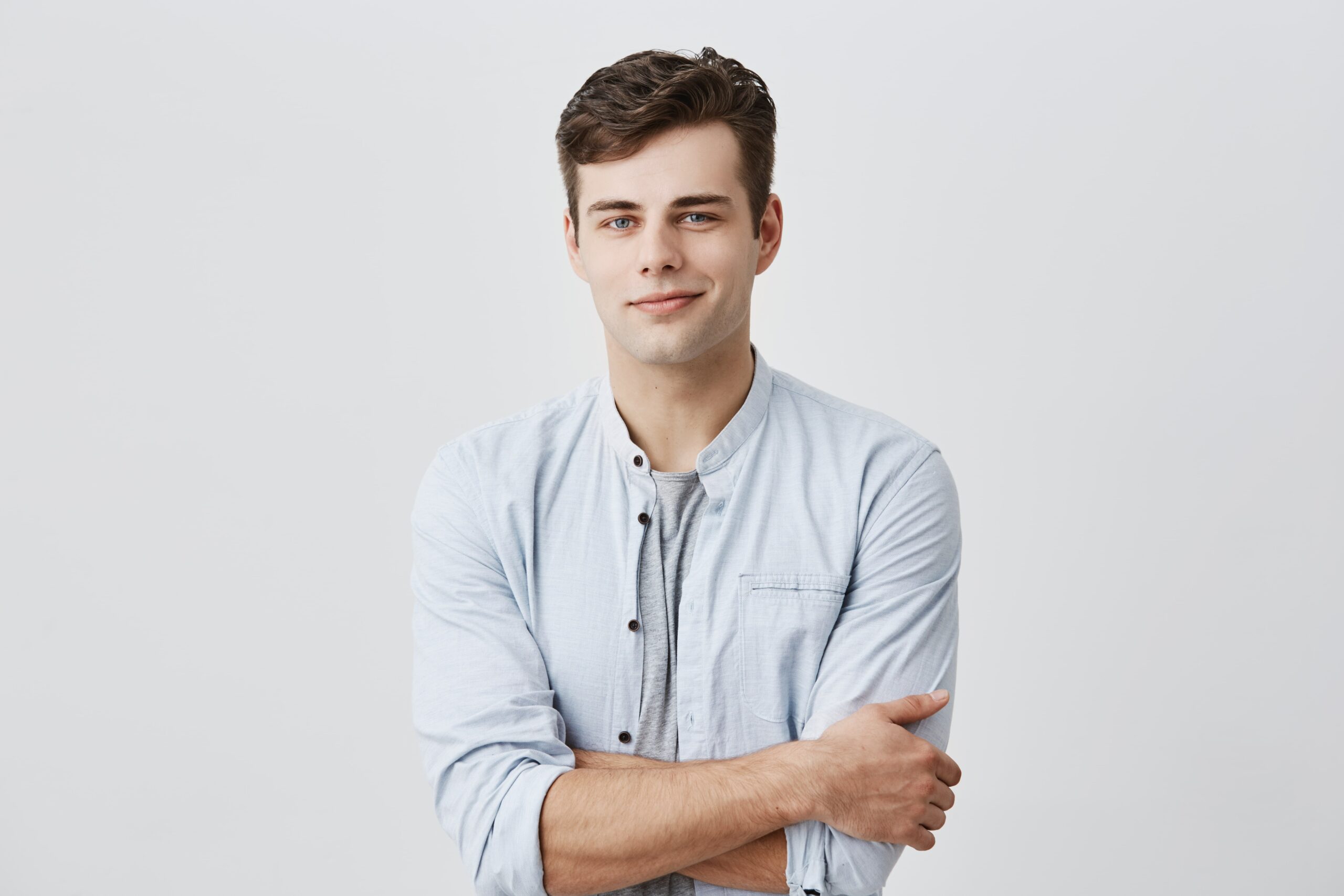 handsome attractive young european man casual shirt with dark hair blue eyes keeping arms folded confidently looking with pleasant smile face expression min scaled