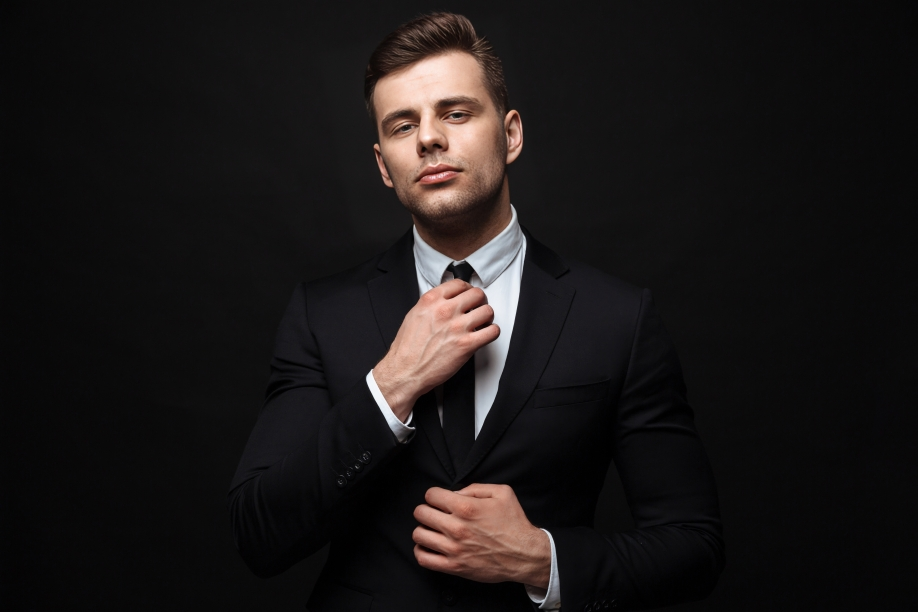handsome confident businessman wearing suit standing isolated black wall posing