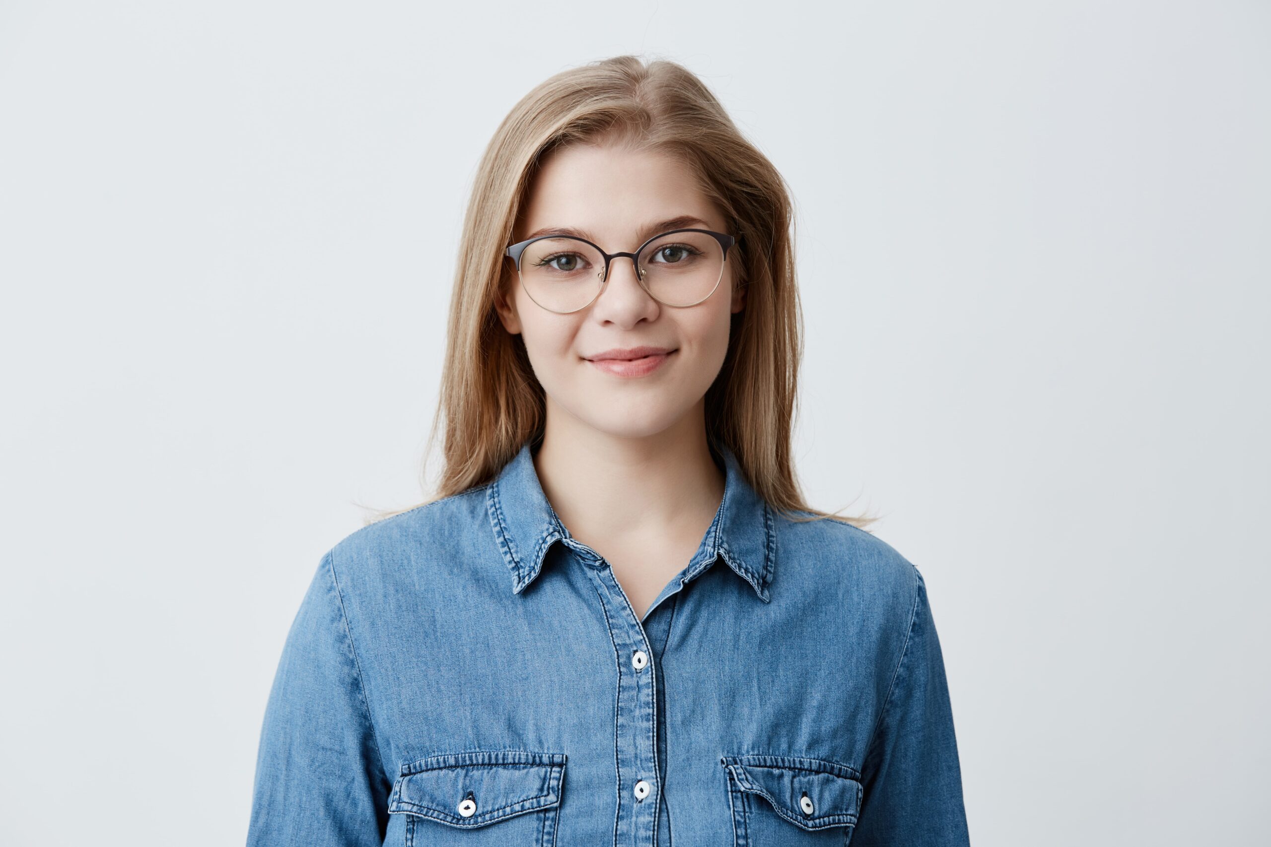 horizontal portrait smiling happy young pleasant looking female wears denim shirt stylish glasses with straight blonde hair expresses positiveness poses min scaled