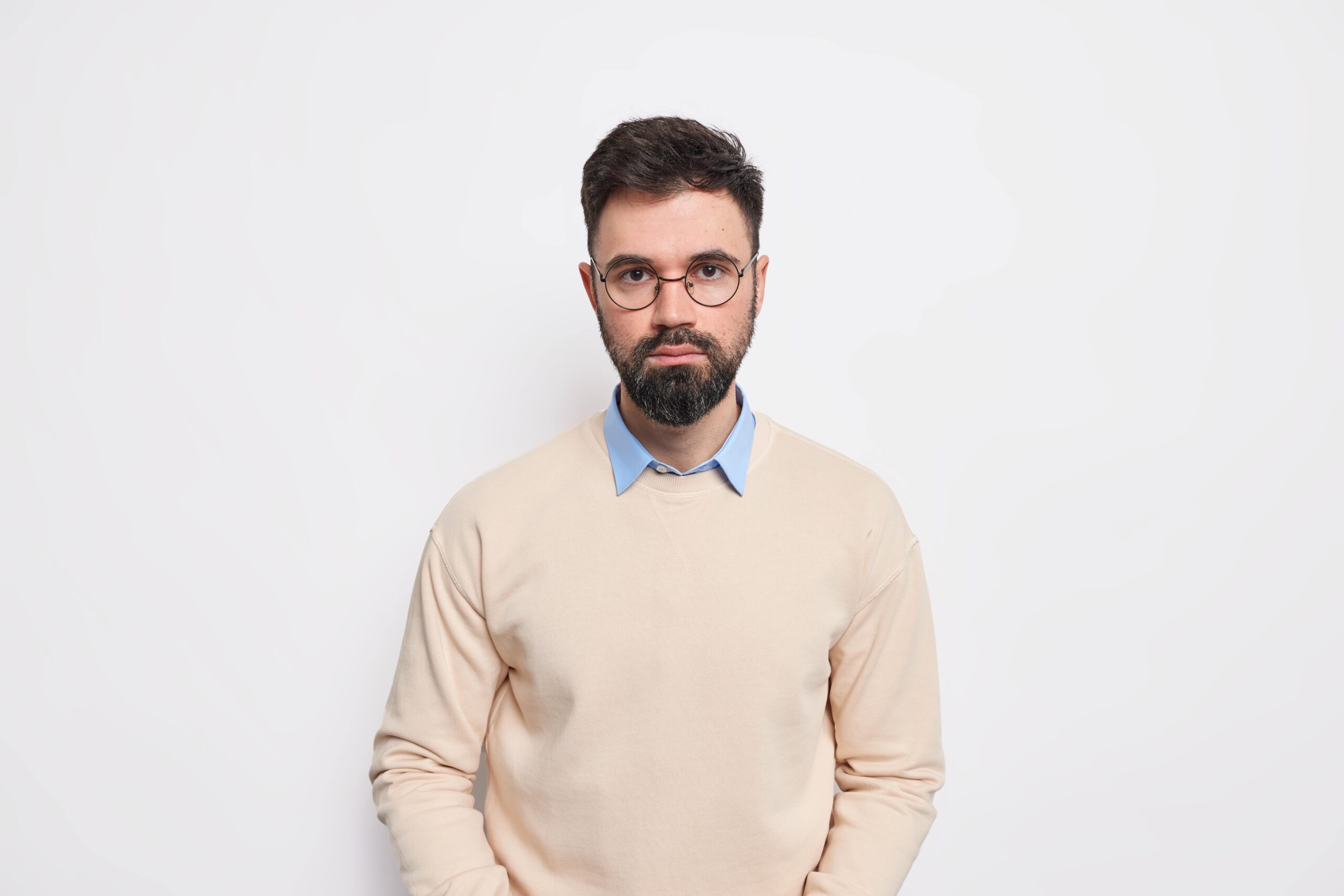 studio shot handsome bearded adult european man looks directly with serious expression has determined face dressed neat jumper round spectacles min scaled