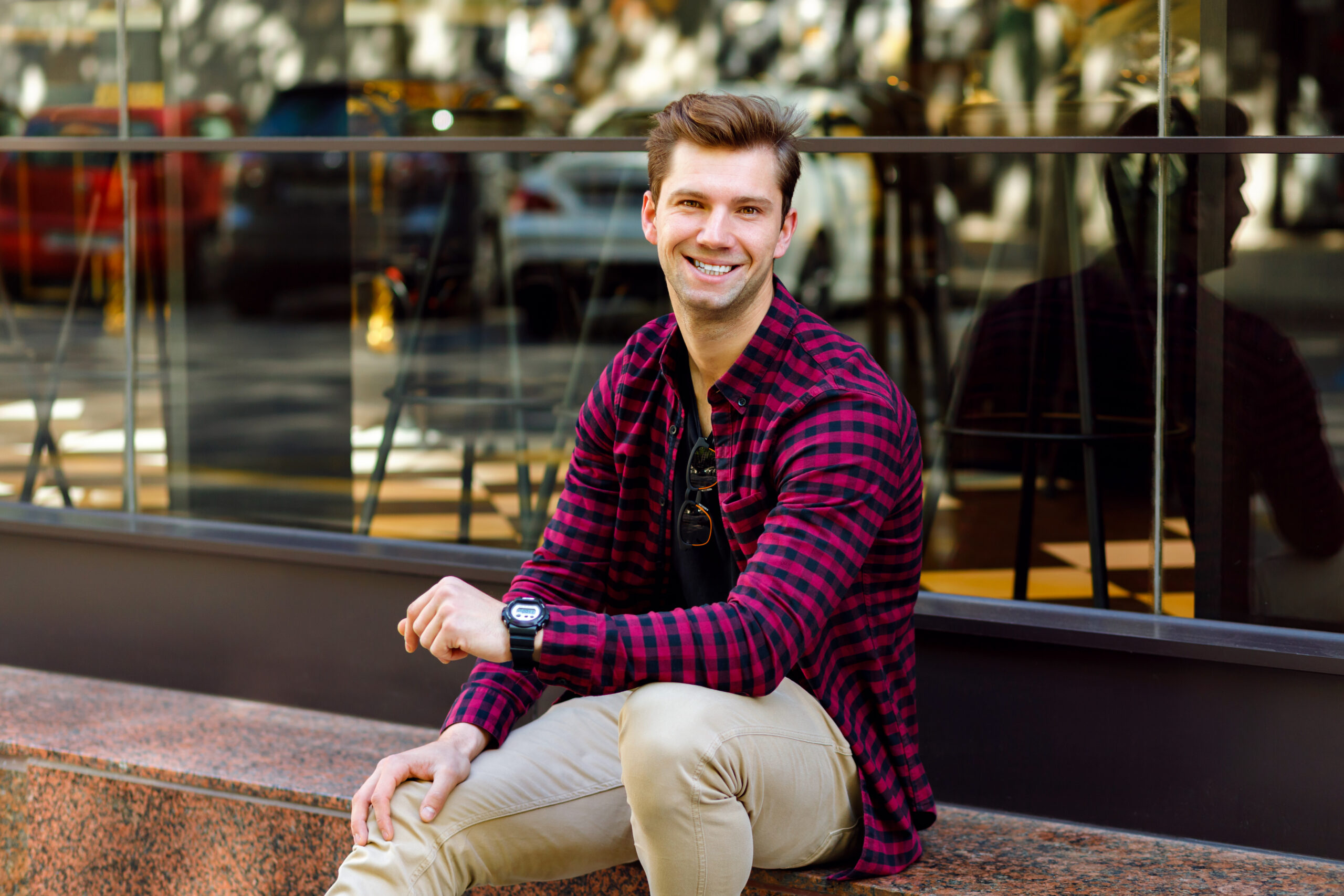 stylish handsome young businessman sitting street amazing smile brown hairs eyes wearing hipster plaid shirt beige trousers sunglasses watches posing near restaurant scaled