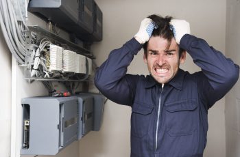 close-up-frustrated-male-electrician-standing-near-electric-board-min