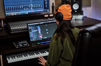 young-woman-female-artist-looking-focused-while-playing-keyboard-synthesizer-sitting-recording-min